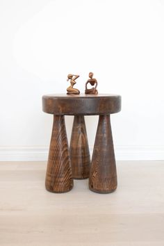 two wooden stools with small figurines sitting on top of them in front of a white wall