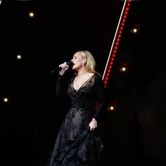 a woman in a black dress singing into a microphone on stage with lights behind her