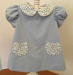 a blue dress with white flowers on the collar and sleeves is sitting on a stand