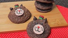 three cookies decorated to look like cats on top of each other, sitting on a wooden board