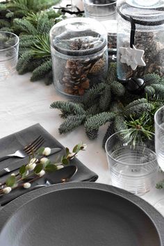 the table is set with pine cones and evergreen branches