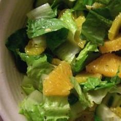 a salad with oranges and lettuce in a white bowl