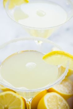 two glasses filled with lemonade sitting on top of a table next to sliced lemons