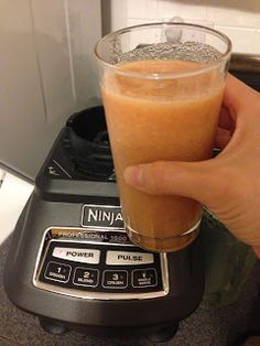 a person is holding a drink in front of a blender