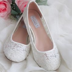 a pair of white wedding shoes sitting on top of a bed next to pink roses