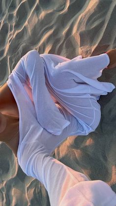 a woman laying on top of a sandy beach next to the ocean with her feet in the sand