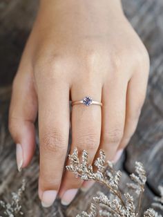 a woman's hand with a ring on it and some flowers in the background