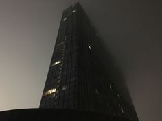 a very tall building in the fog with lights on it's sides and windows