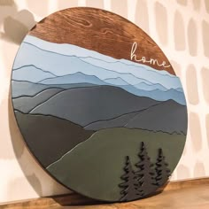 a wooden plaque with mountains and trees painted on it