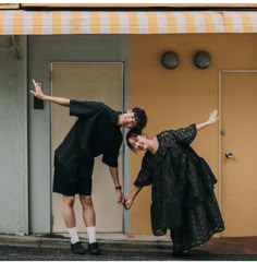 two people standing in front of a building with their arms out and one person reaching for the other