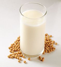 a glass of milk with chickpeas scattered around it on a white surface,