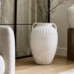 a white vase sitting on top of a wooden floor next to a mirror and chair