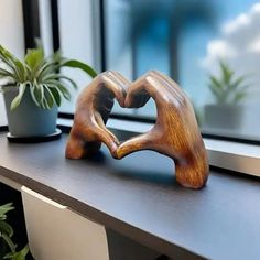 two wooden hands making a heart shape on a window sill next to a potted plant