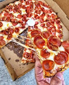 a pepperoni pizza is being held up by someone's hand with one slice missing