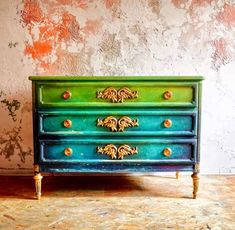 a green and blue dresser sitting on top of a wooden floor next to a wall