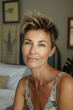 Woman with short spiky hair, smiling softly, sitting indoors.