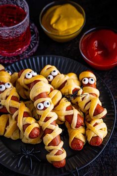 hotdogs wrapped in yellow paper with googly eyes and mouthballs on a black plate