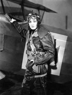 black and white photograph of woman in pilot's outfit standing next to an airplane