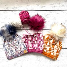 three knitted hats with pom - poms on top of white wooden boards