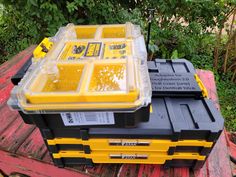 a yellow and black tool box sitting on top of a wooden table next to trees