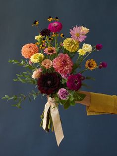 a bouquet of colorful flowers tied to a yellow ribbon on a blue background with a person's hand holding it