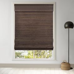 a room with a window covered in brown roman shades and a lamp next to it