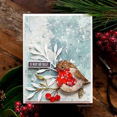 a close up of a christmas card on a wooden table with holly and pine cones