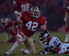 two football players are on the field with one running for the ball and another laying on the ground