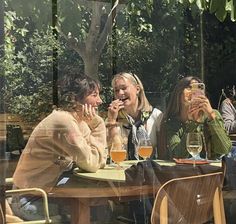 three women sitting at a table with wine glasses in front of them and one woman holding her mouth open