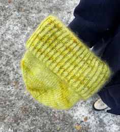 a person is wearing a yellow knitted mitt and standing on the sidewalk with their feet in the snow