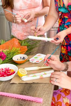 three women standing at a table with food and utensils in their hands,