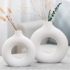 two white vases with plants in them sitting on a table next to a couch