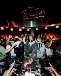 a dj mixing in front of a large group of people at a party with their hands up