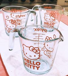 four hello kitty measuring cups sitting on top of a white tablecloth with hello kitty decals