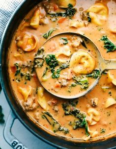 a spoon full of soup with dumplings and spinach in it, on top of a blue cloth