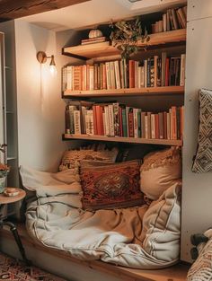 a book shelf filled with lots of books next to a bed covered in blankets and pillows