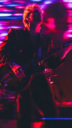 a man playing a guitar on stage with bright lights in the backgrouund