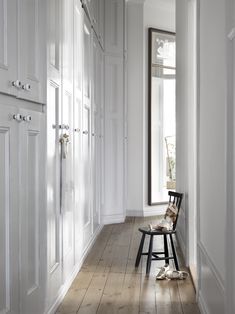 an empty hallway with white walls and wooden flooring is pictured in this image, there are two chairs on either side of the hall