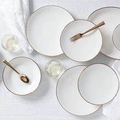 white plates with gold rims are arranged on a table cloth, next to silverware and utensils