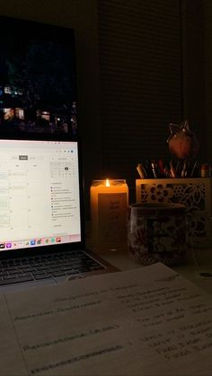 an open laptop computer sitting on top of a desk next to a candle and cup