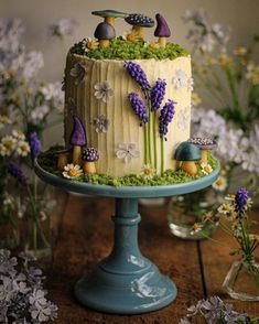 a cake decorated with flowers and mushrooms is on a blue pedestal in front of some wildflowers