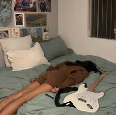 a woman laying on top of a bed next to an electric guitar and pillows with pictures above her