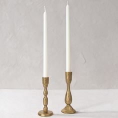 two gold candlesticks with one candle in the middle and one on the other