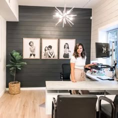 a woman standing at a desk in an office with pictures on the wall behind her