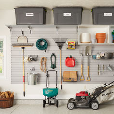 a garage with several storage bins and various tools hanging on the wall next to a lawn mower