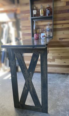 a wooden table sitting on top of a floor next to a shelf filled with bottles