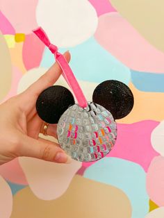 a hand holding a mickey mouse ornament in front of a colorful background with circles