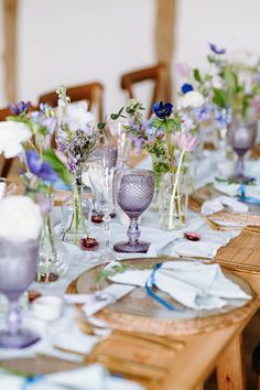 the table is set with purple and white flowers in vases, silverware, and napkins