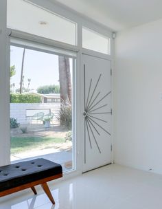 a white room with a bench in front of the door and palm trees behind it