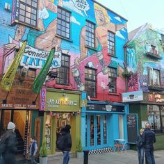 several people are walking on the sidewalk in front of some buildings with colorful painted walls